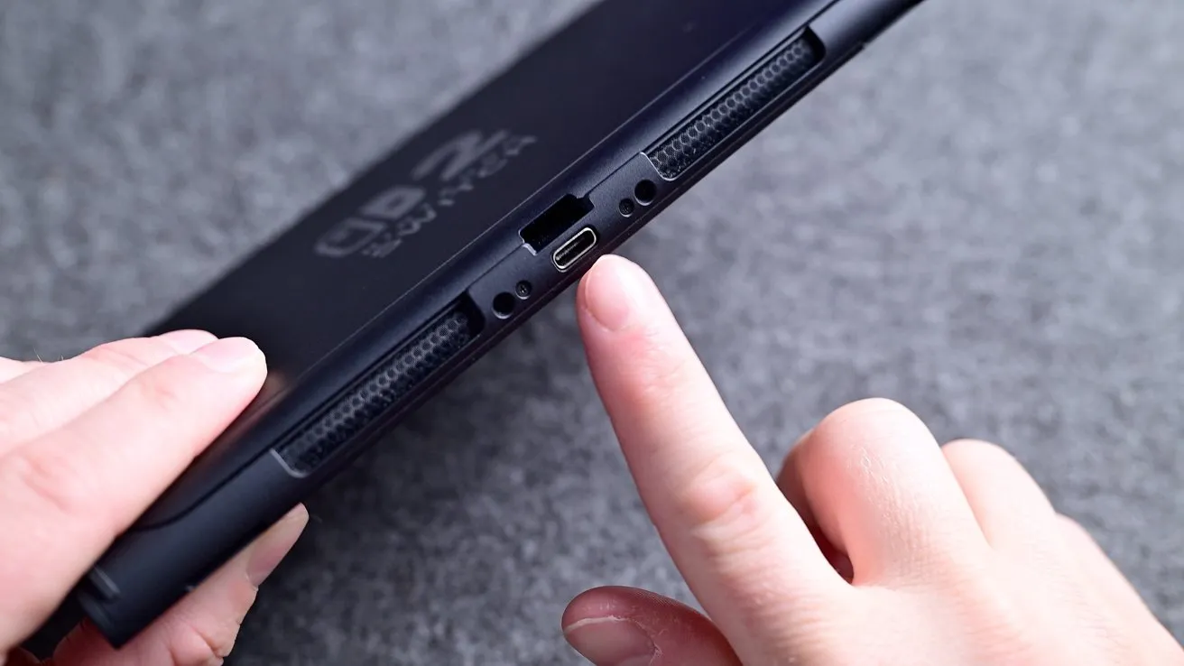 دست که به پورت USB-C دستگاه اشاره می‌کند روی سطح خاکستری رنگ