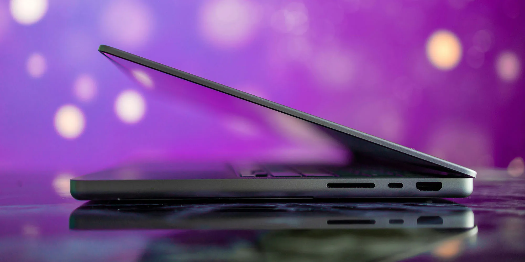 MacBook Pro با نمای نیمه‌باز در پس‌زمینه بنفش